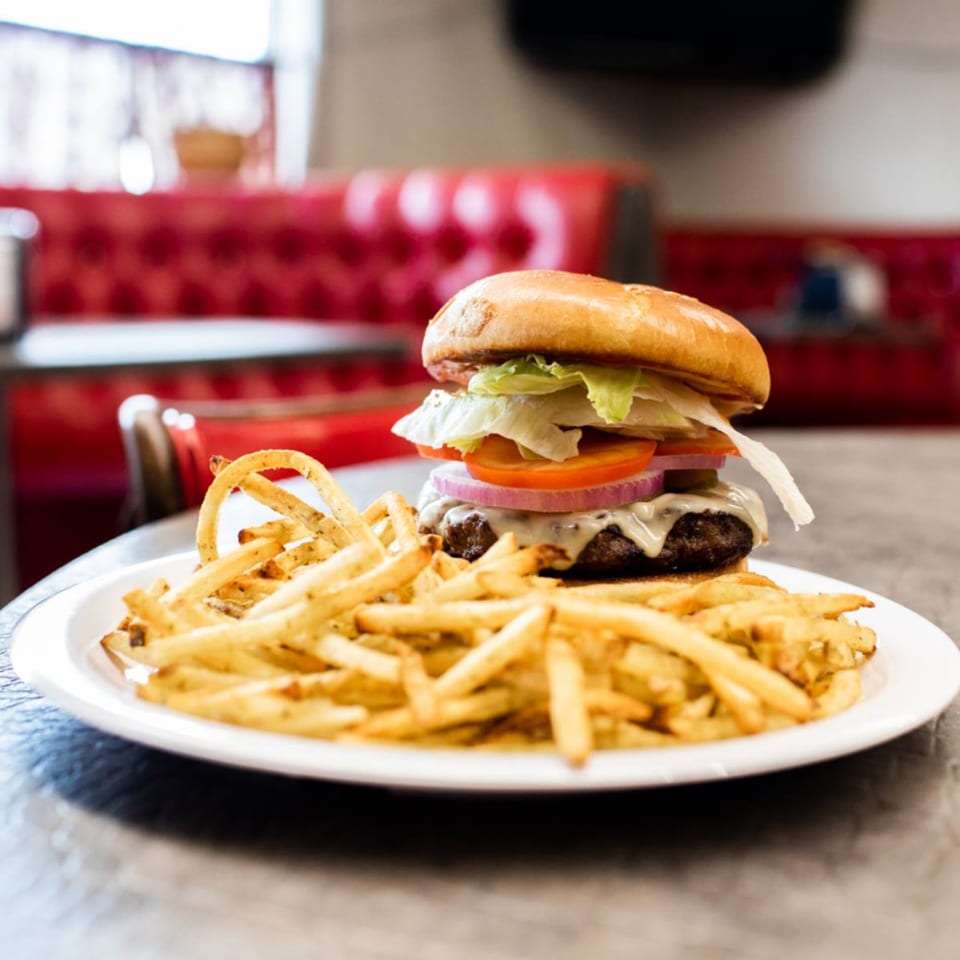 A cheeseburger with lettuce, tomato, and onion, served with a side of fries on a white plate.