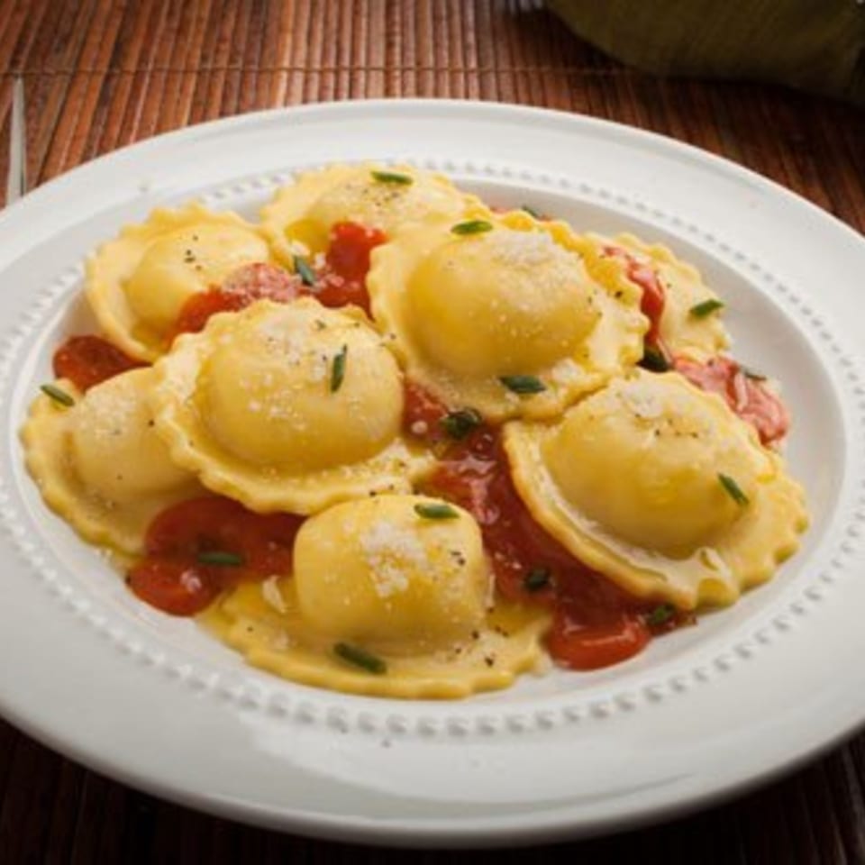Plate of ravioli with red sauce, sprinkled with cheese and herbs, on a white plate.