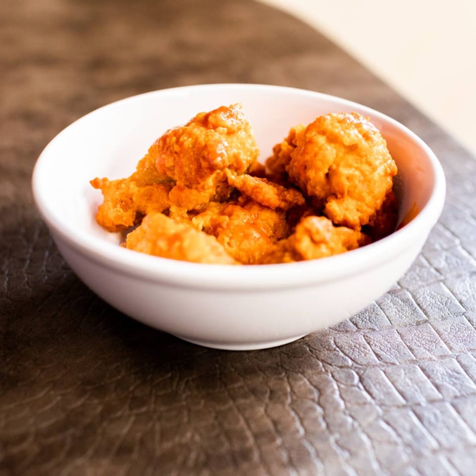 A white bowl filled with golden-brown, saucy boneless chicken wings from Slice of Veyo.